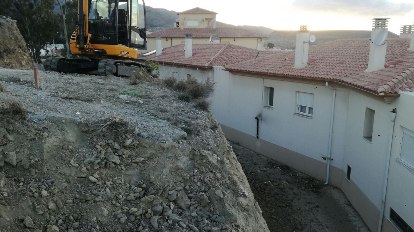 Talud inicial sin tratar en Tíjola con miniexcavadora JCB ya colocada al atardecer