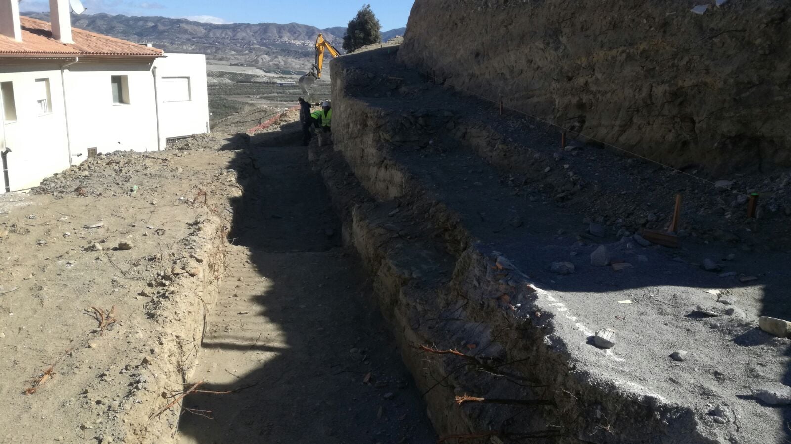 Rebaje de talud urbano en Tíjola con casas blancas residenciales y montañas al fondo, ejecutado por Excavaciones Tripiana