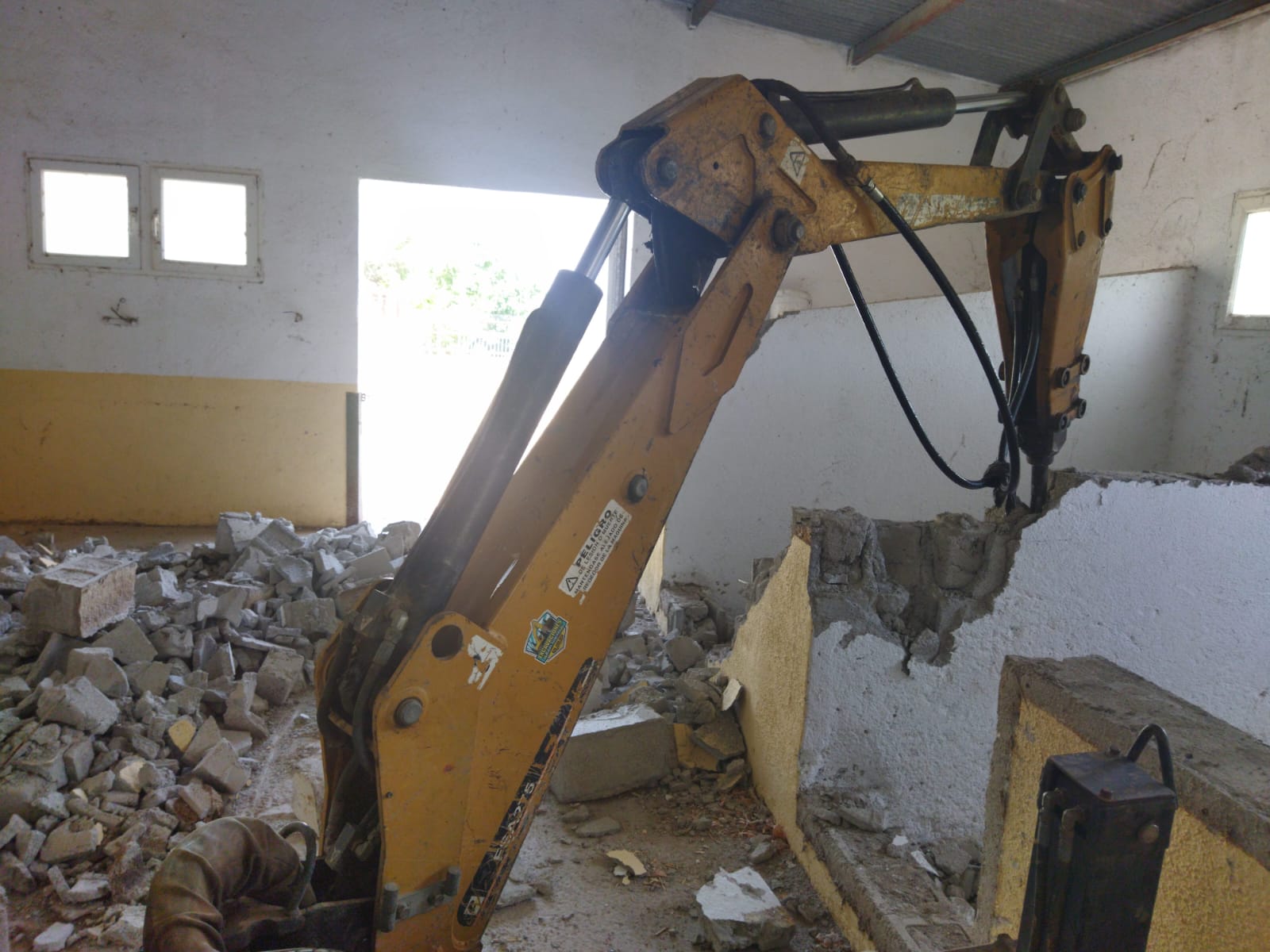 Demolición avanzada del tabique interior con pala mecánica empujando los bloques